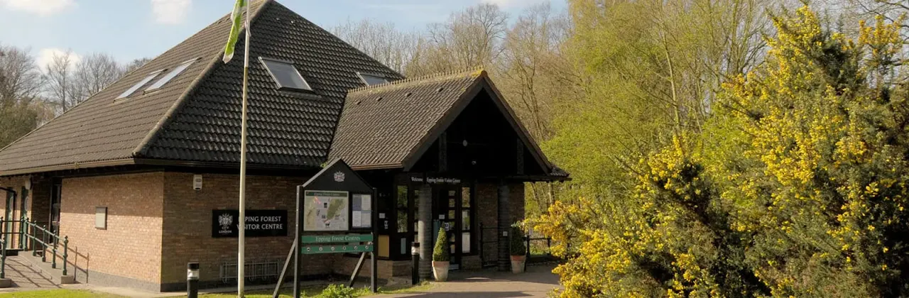 Modern brick visitor centre building with dark tiled roof surrounded by trees in early spring foliage.