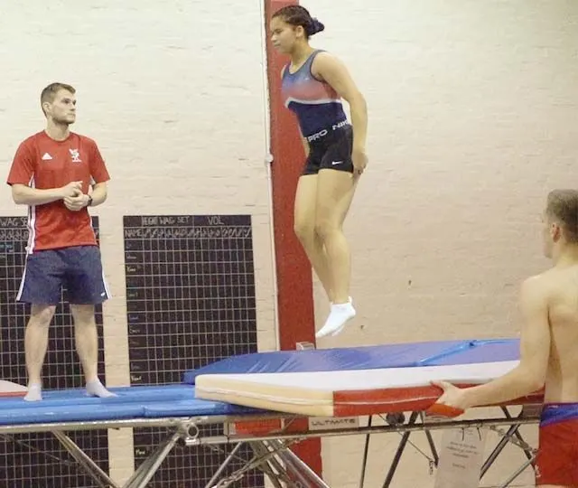Young gymnasts training on trampolines with an instructor in a gym hall.
