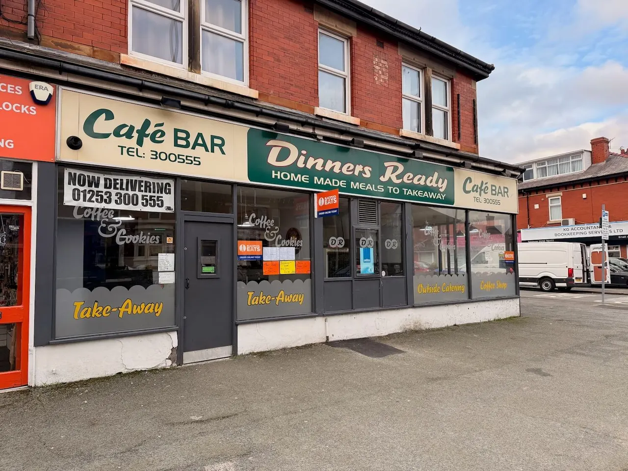Storefront of a café bar offering takeaway coffee, cookies and home-made meals, with red brick building above.