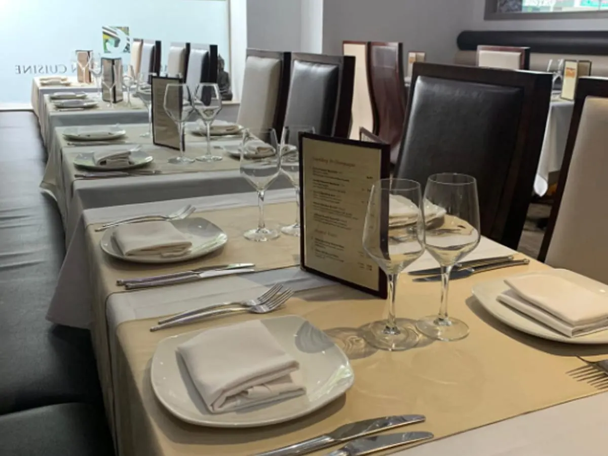 Formal dining table set with place settings, napkins, glasses and menu card for restaurant service.