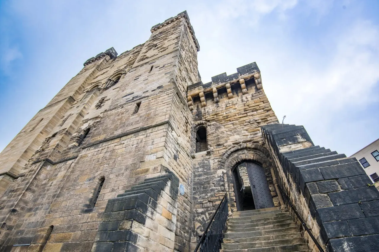 Historic stone castle towers with crenellations and narrow windows, photographed from ground level against a blue sky.