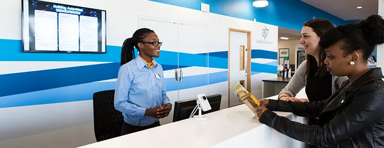 Staff member in blue shirt speaks with two visitors at the reception desk.