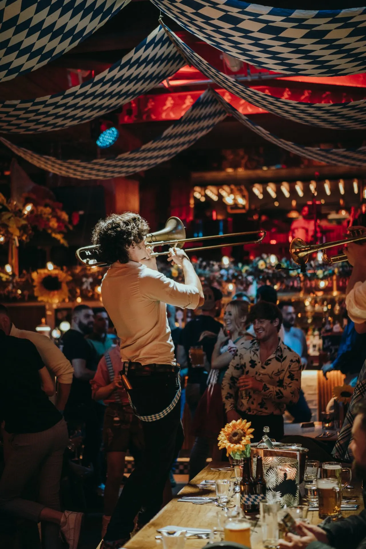 Musician playing trombone at an indoor event with diners seated at tables under blue and white patterned fabric canopies.