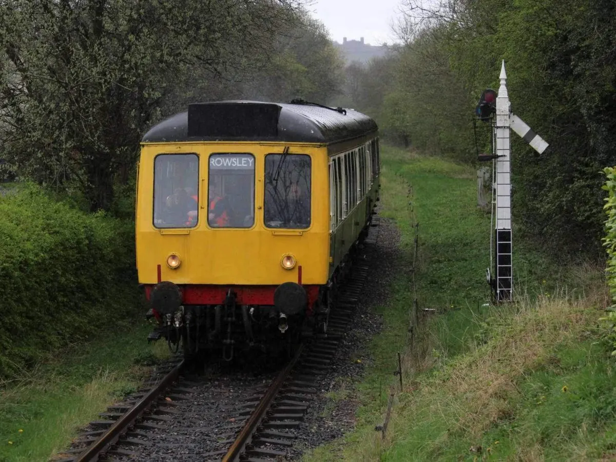 Yellow and red heritage railway train travelling through tree-lined countryside with a signal box visible on the right.
