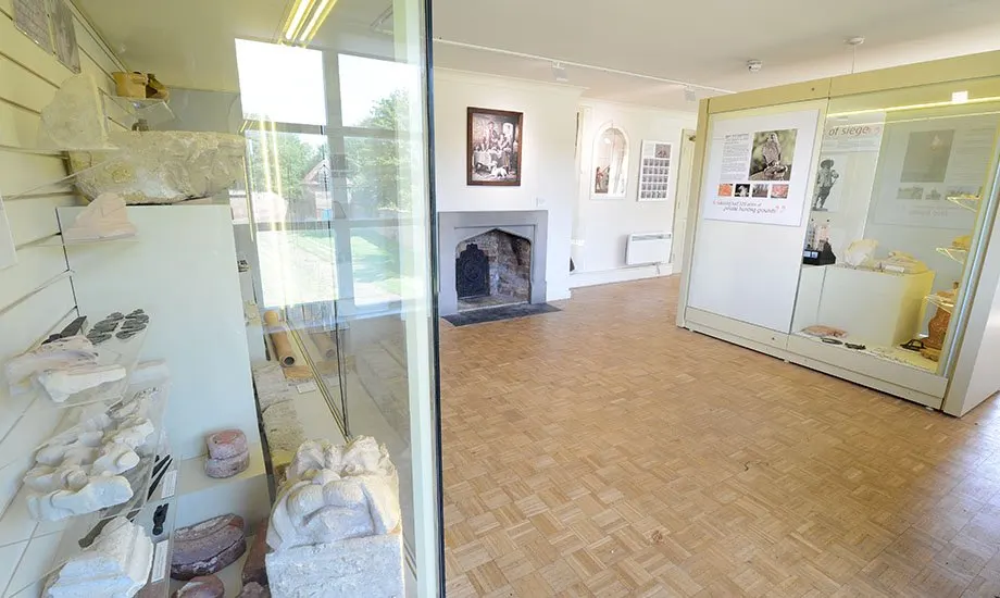 Interior of a museum gallery displaying artefacts in glass cases, with a fireplace and informational displays on cream walls.