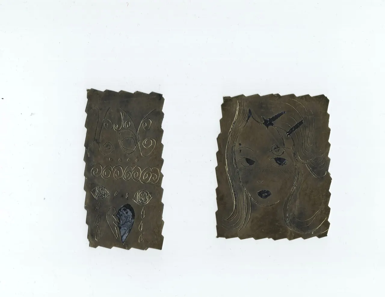 Two engraved metal plaques with abstract faces and decorative patterns against a white background.