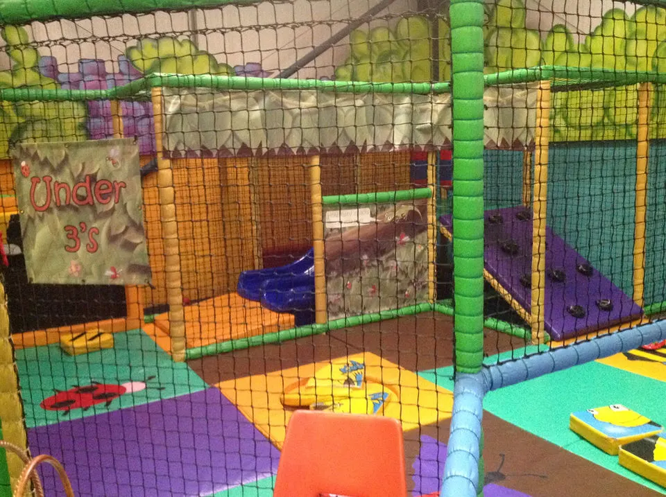 Colorful indoor soft play area for young children, with padded foam structures, netting, and an "Under 3's" section visible.