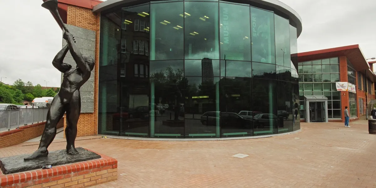 Modern brick and glass building with a bronze figure sculpture in the foreground courtyard.