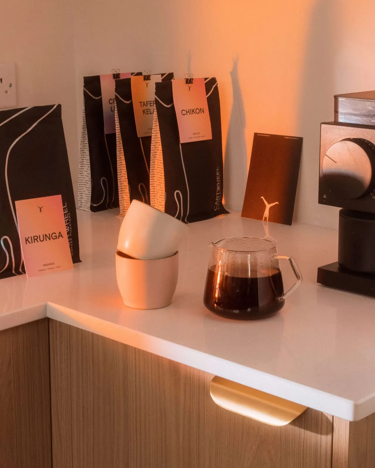 Coffee shop display with packaged beans, a ceramic cup, and glass carafe on a white counter, warmly lit.