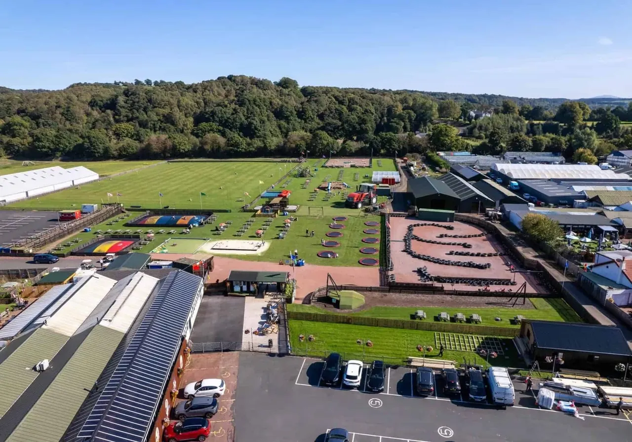Aerial view of a sports and leisure facility with multiple activity areas including inflatable obstacles, climbing walls, grass fields and woodland surroundings.