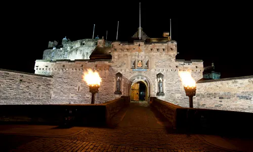 The Gatehouse entrance to Edinburgh Castle illuminated at night, with stone walls and lamp posts.