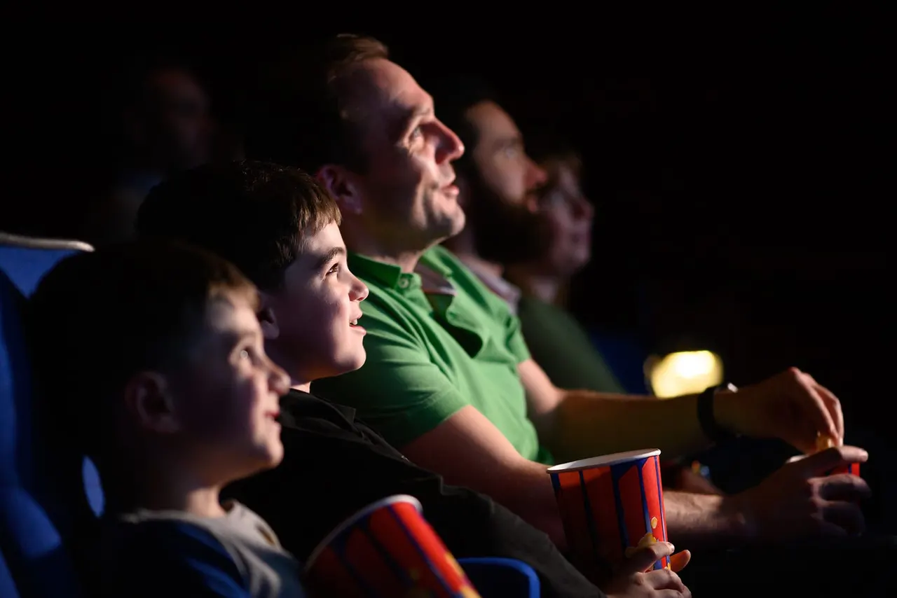 Group of people watching a film in a cinema, holding popcorn boxes and looking engaged.