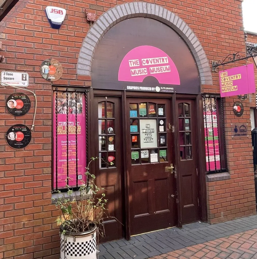 Red brick building entrance with pink signage for a music museum, featuring arched doorway and vinyl record decorations on the facade.
