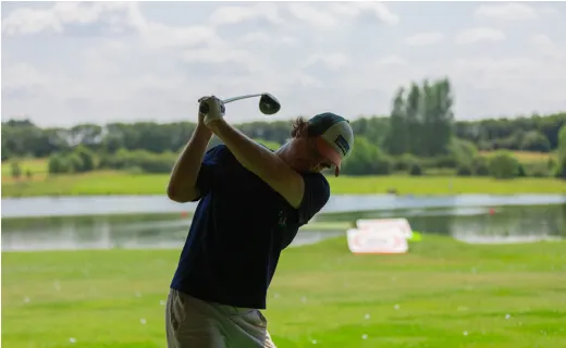 Golfer mid-swing on a course with a lake and green landscape behind.