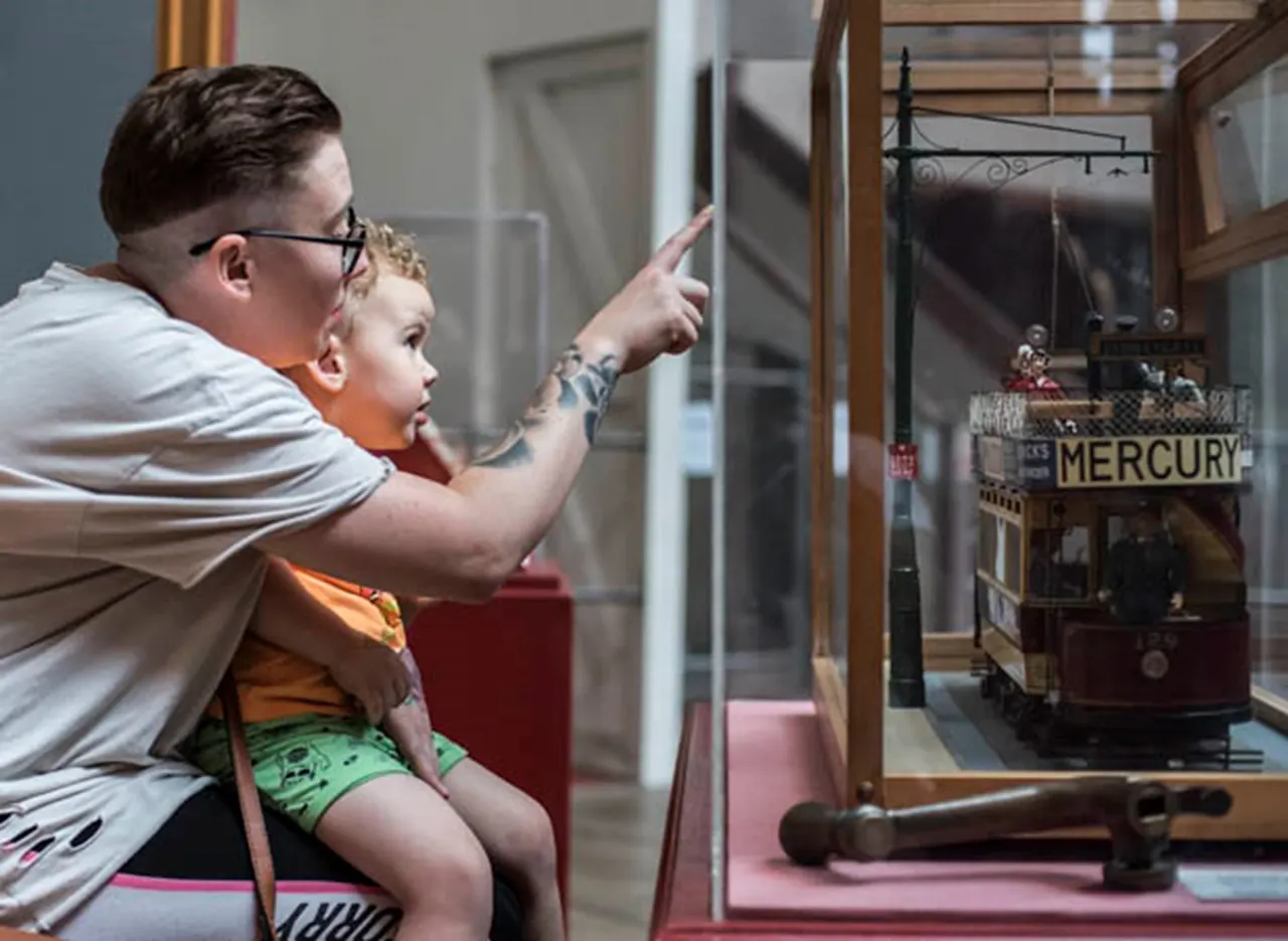 An adult and child viewing a model ship labelled Mercury in a museum display case.