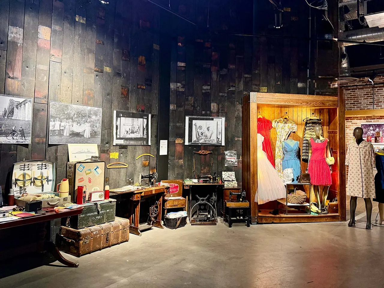 Museum interior displaying vintage clothing on mannequins, antique furniture, historical photographs and memorabilia arranged in wooden display cases.