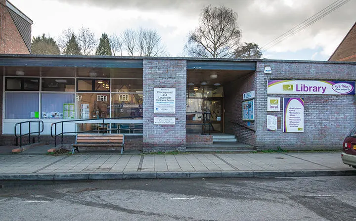 Brick-built library building with glass frontage, bench seating outside and bare winter trees beyond.