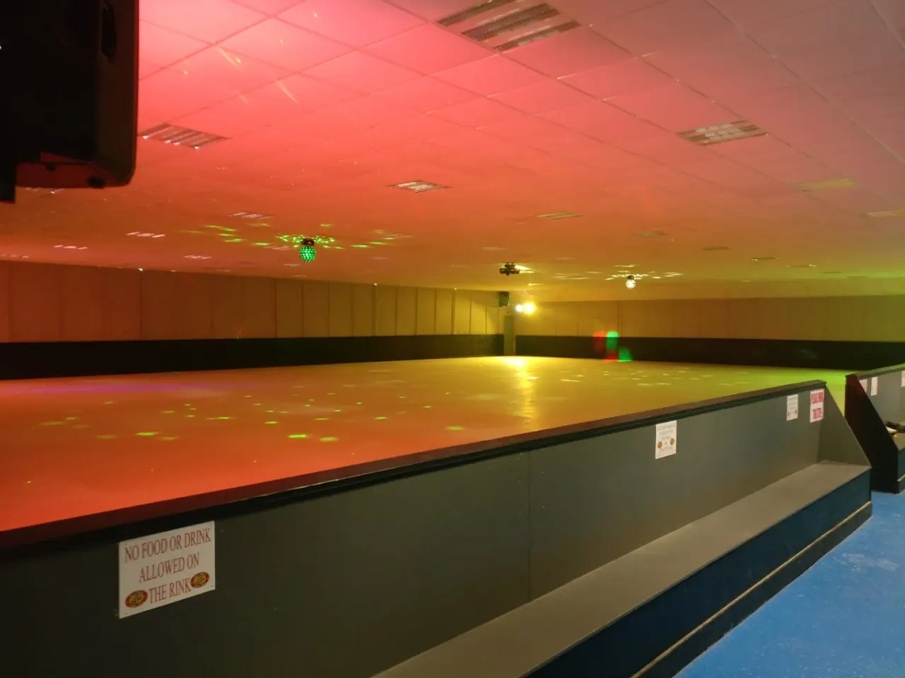 Empty indoor skating rink with colourful mood lighting in red, orange and green hues.