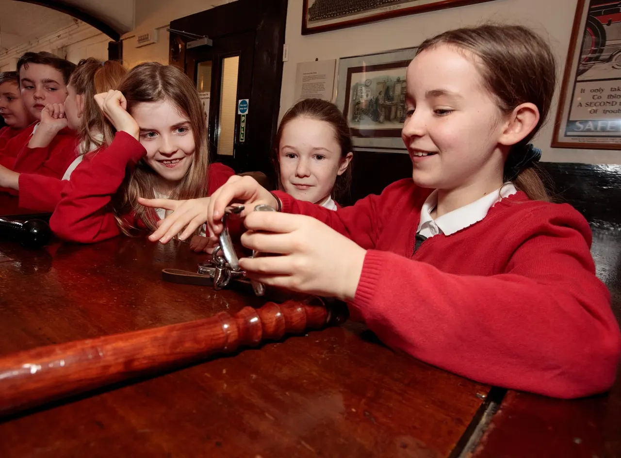 Children in school uniforms examining a vintage police weapon on display in a museum interior.