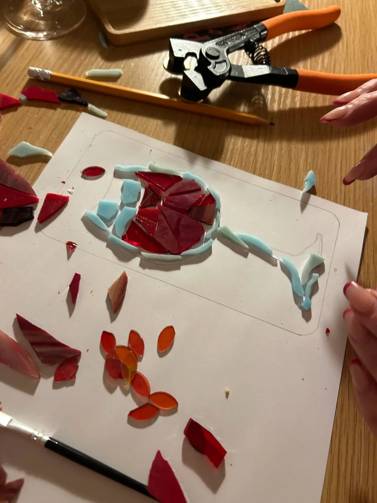 Hands arranging cut flower petals and pale blue clay shapes on white paper during a creative craft workshop.
