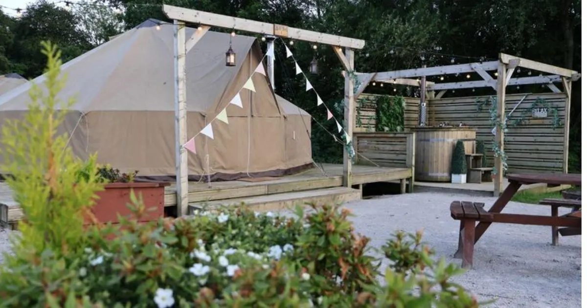 Glamping bell tents with wooden pergolas and bunting in a rural camping ground surrounded by greenery.