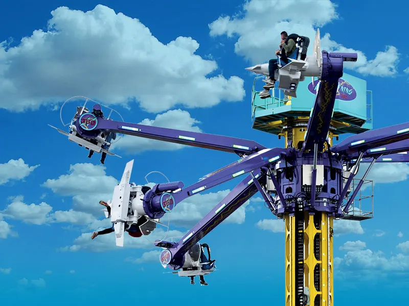 Riders on a spinning fairground ride with multiple colourful arms against a bright blue sky with white clouds.