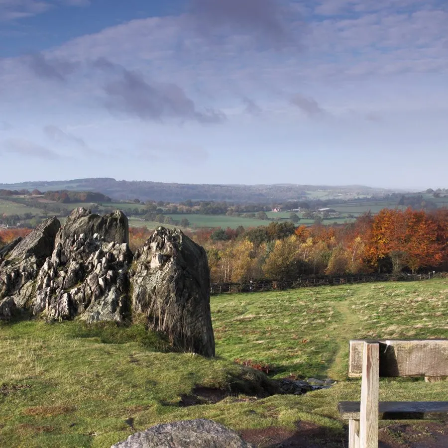 Rocky outcrop in a green pasture with autumn woodland and rolling countryside beyond.
