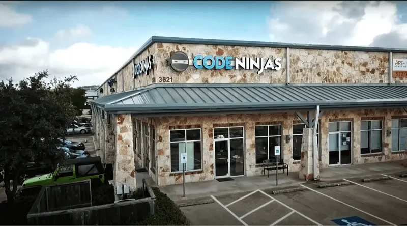 This is a PHOTOGRAPH.

A Code Ninjas storefront building with stone exterior, metal roof, glass entrance doors, and parking spaces in front.