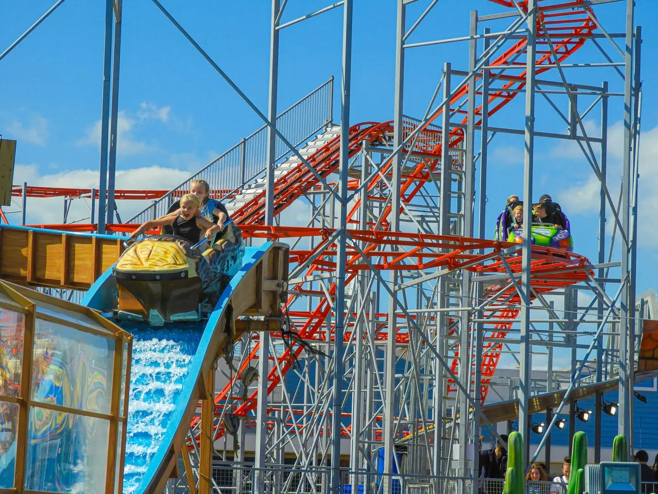 Children riding a water slide at a seaside amusement park on a sunny day.