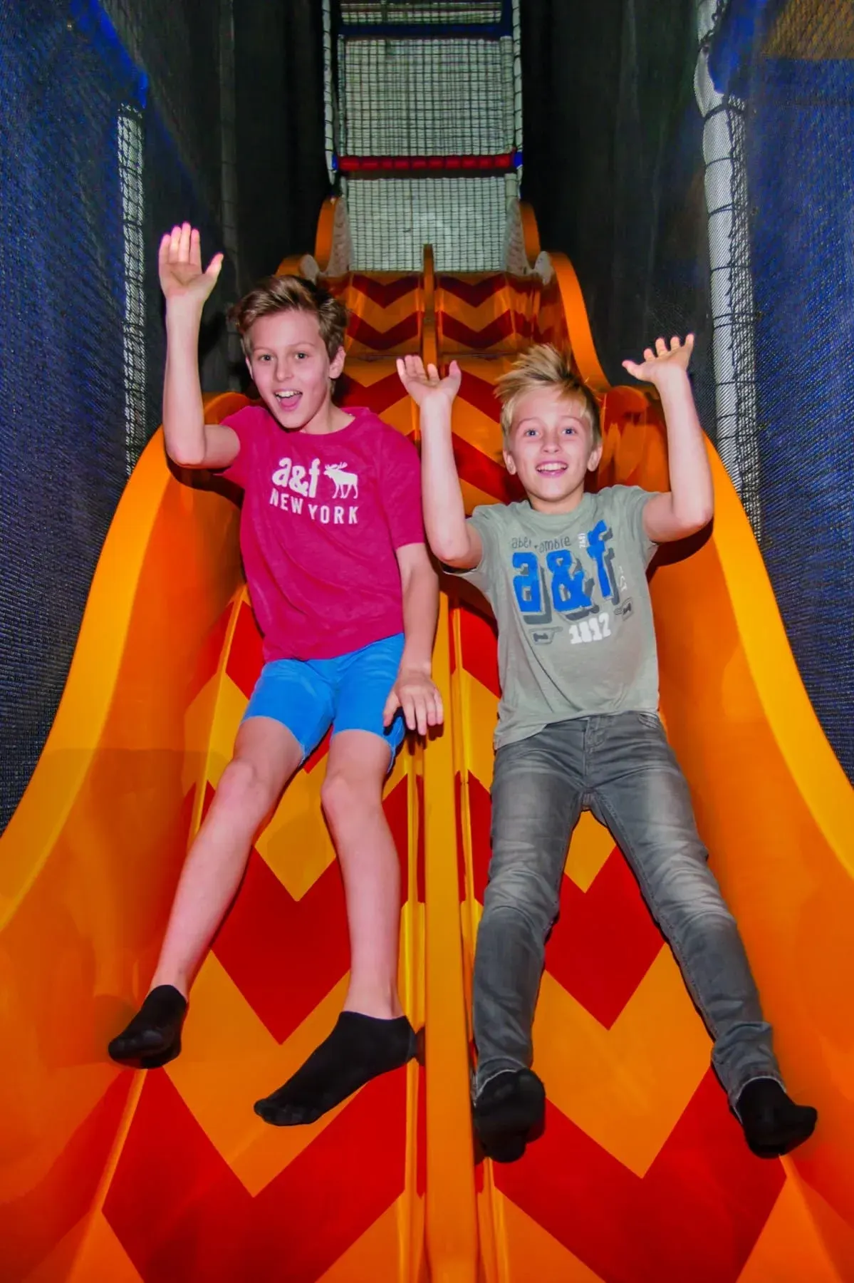 Two children sliding down a large inflatable slide with arms raised, smiling at the camera.