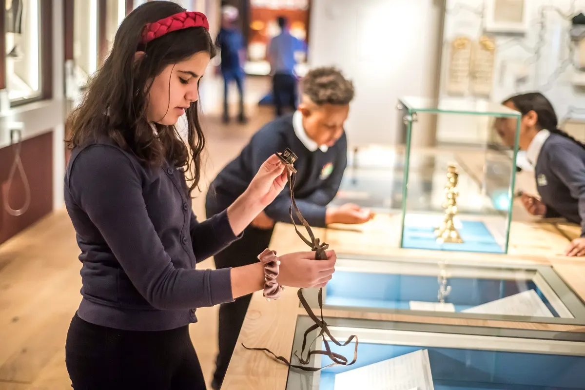 Young woman wearing a red headband examines an artefact on a cord whilst viewing display cases in a museum gallery.