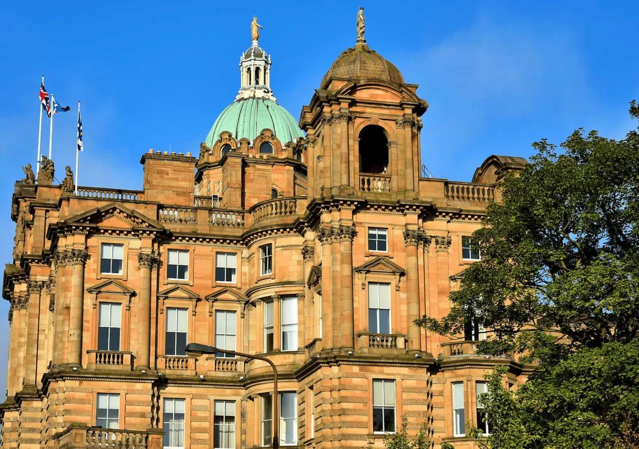Grand Victorian sandstone building with dome and turrets under clear blue sky, featuring classical architecture and flags.