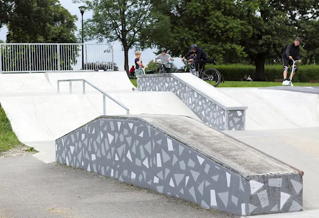 Young people skateboarding and riding bikes on concrete ramps and rails at an outdoor skate park.