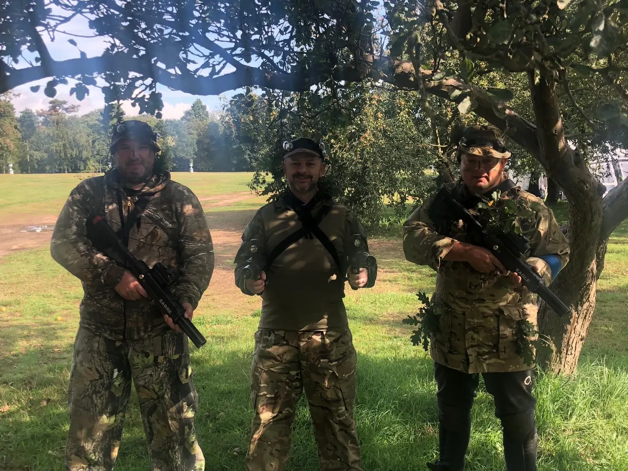 Group of kids and adults in woodland laser tag session posing with rifles
