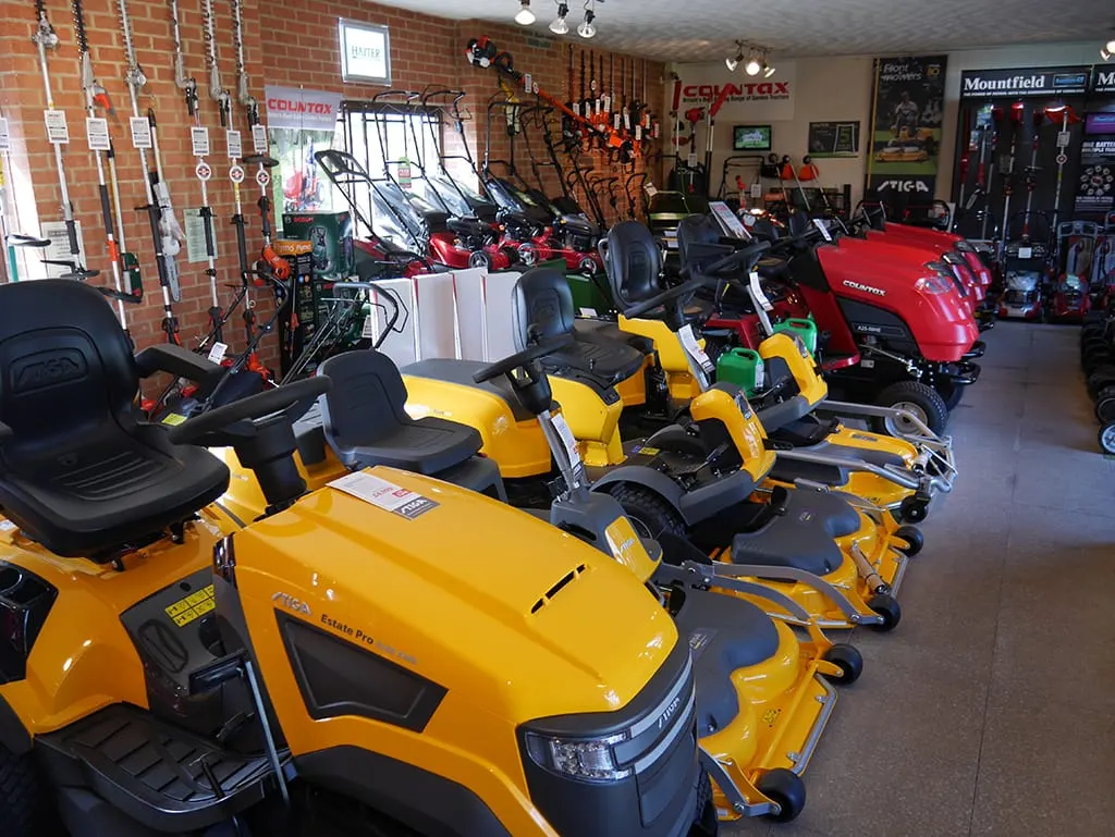 Indoor showroom displaying rows of yellow and red ride-on mowers and garden machinery for sale.