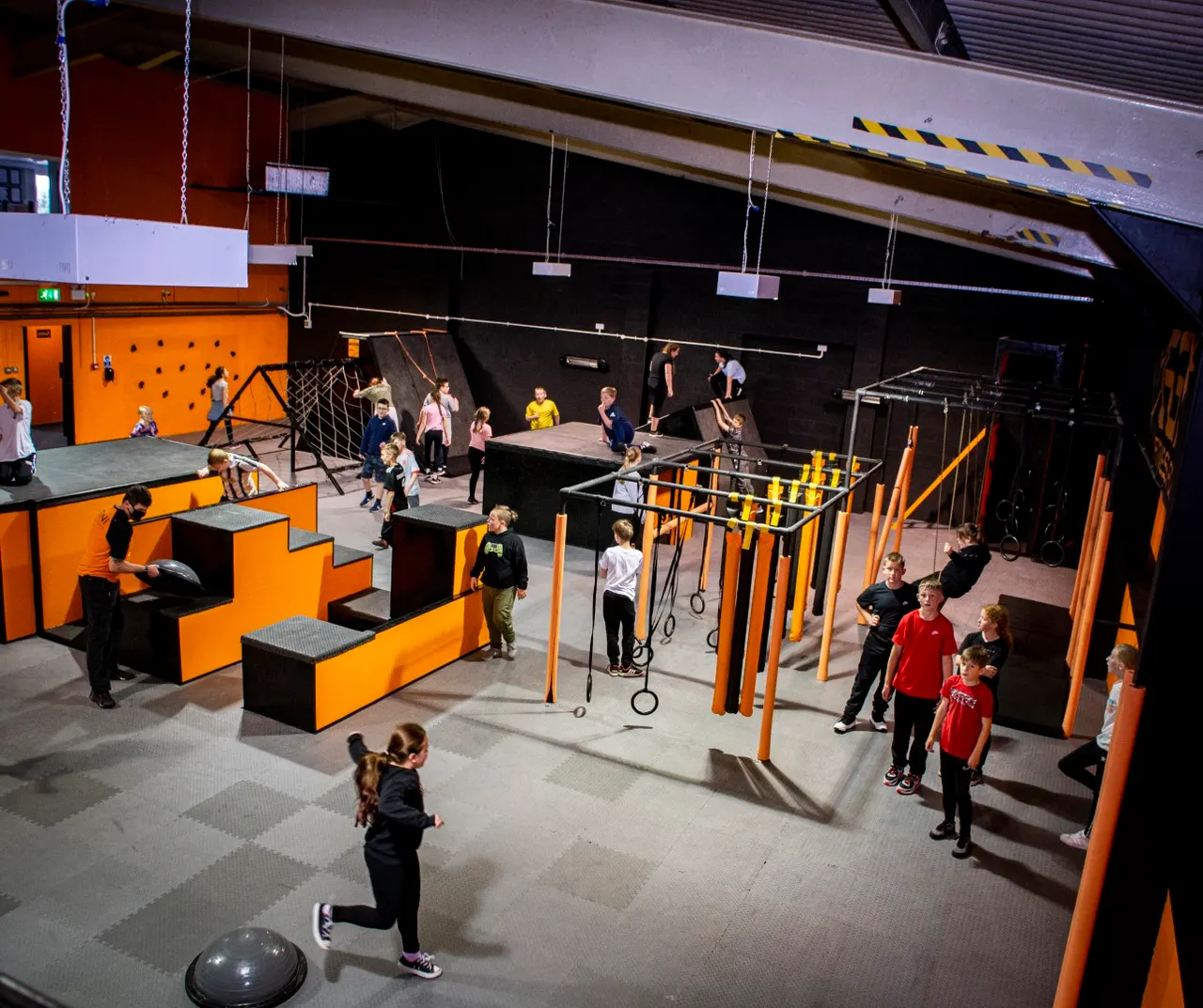 Children using various climbing walls, rope courses, and obstacle equipment in an indoor sports and activity hall.