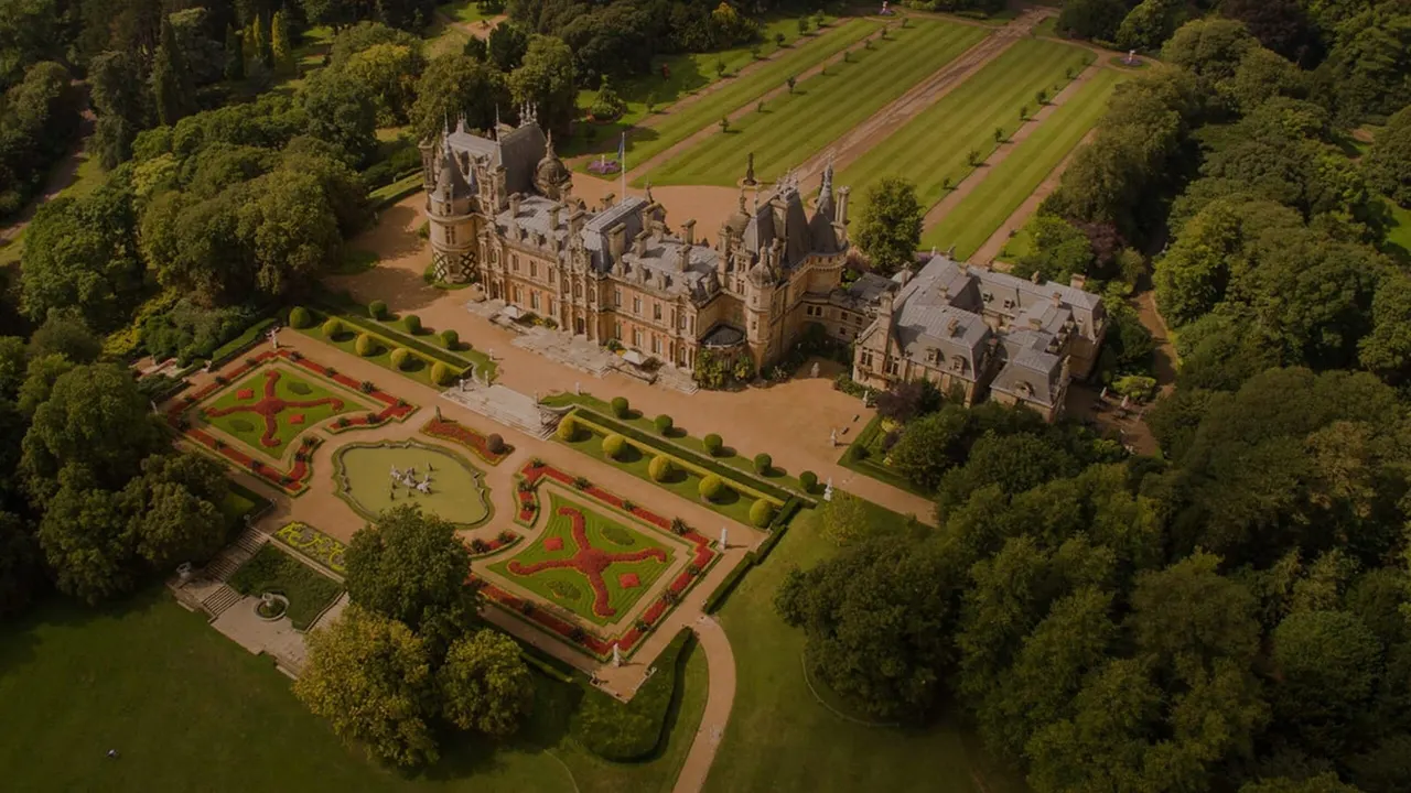 Aerial view of a grand Victorian mansion surrounded by formal gardens with geometric hedges and manicured lawns.
