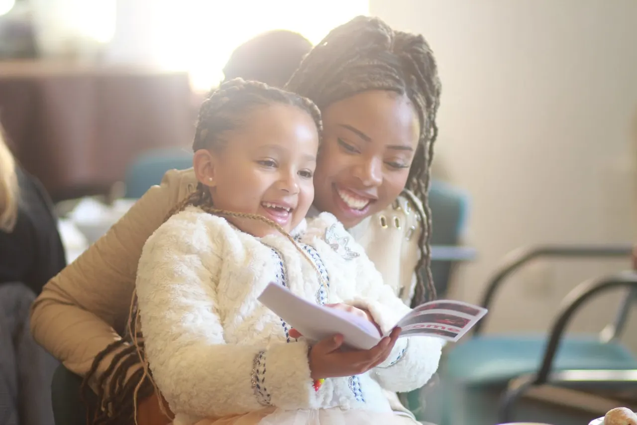 Woman and young child reading a book together indoors, both smiling.