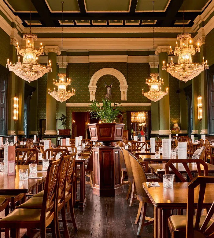 Elegant dining room with wooden tables and chairs, crystal chandeliers, green walls, ornate archway, and classical architectural details.