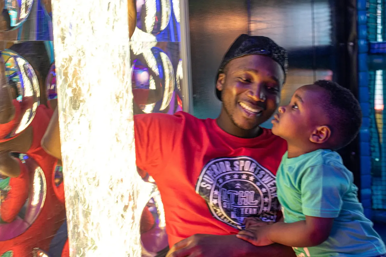 Adult and child looking up at illuminated interactive light display in indoor play venue.