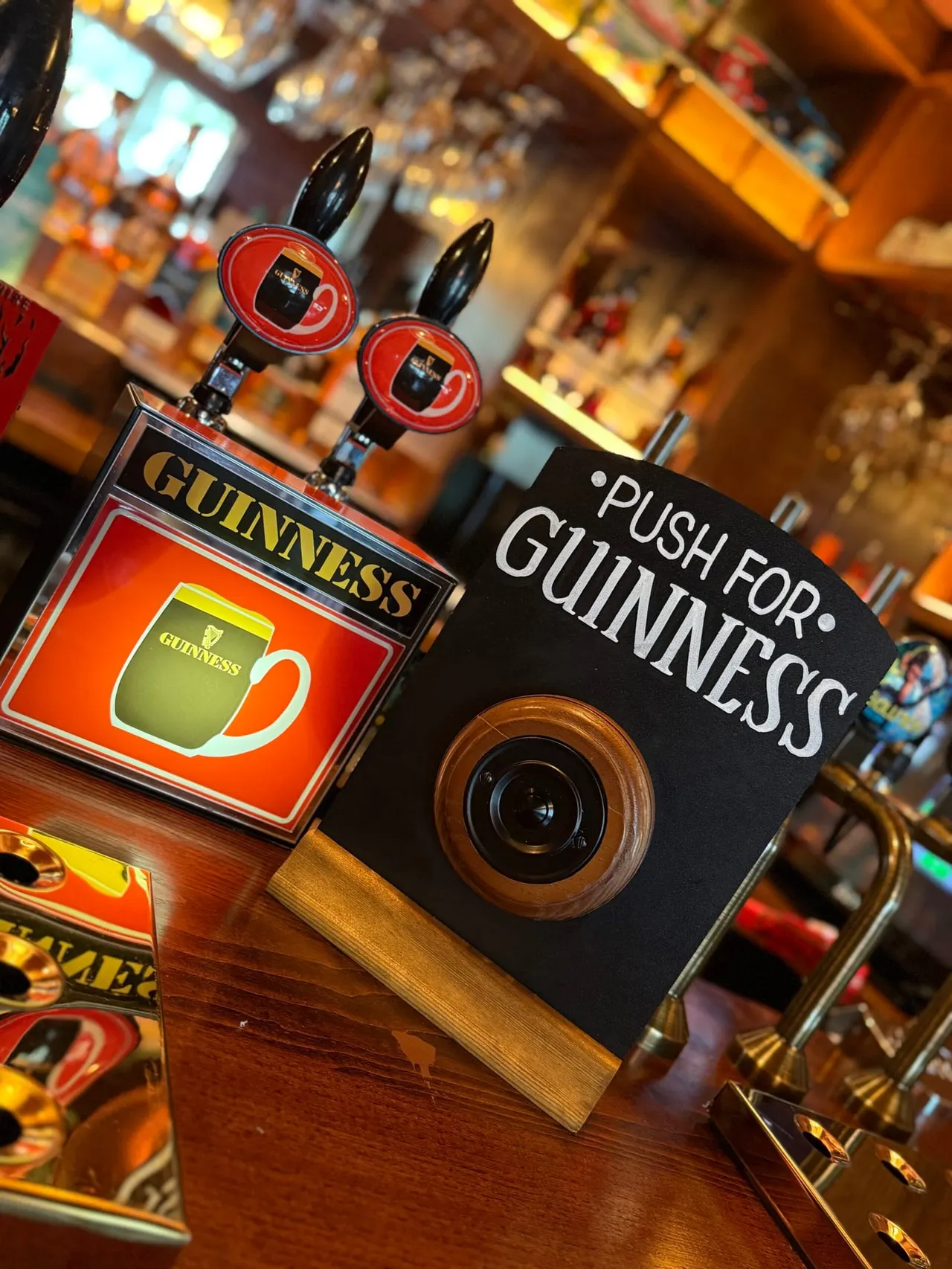 Guinness branded beer pump handles and signage displayed on a wooden bar counter in a pub.