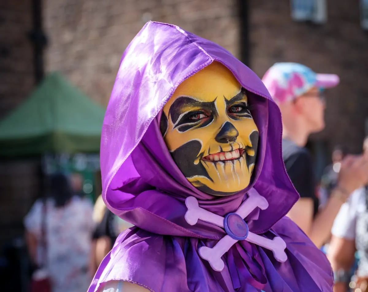 Child in purple skeleton costume and hood at outdoor event near historic stone buildings.