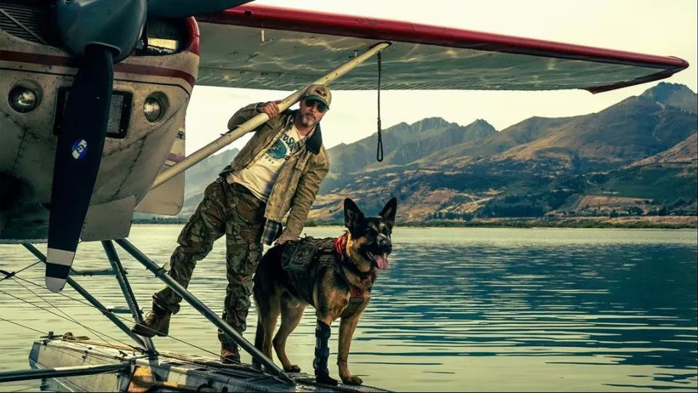 Person and dog boarding a seaplane on a calm lake with mountains in the background.