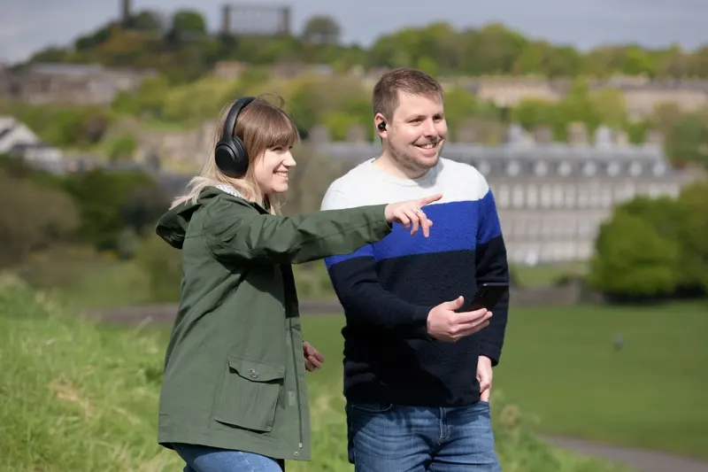 Two people walk together across a grassy hill overlooking Edinburgh's historic buildings and landscape.