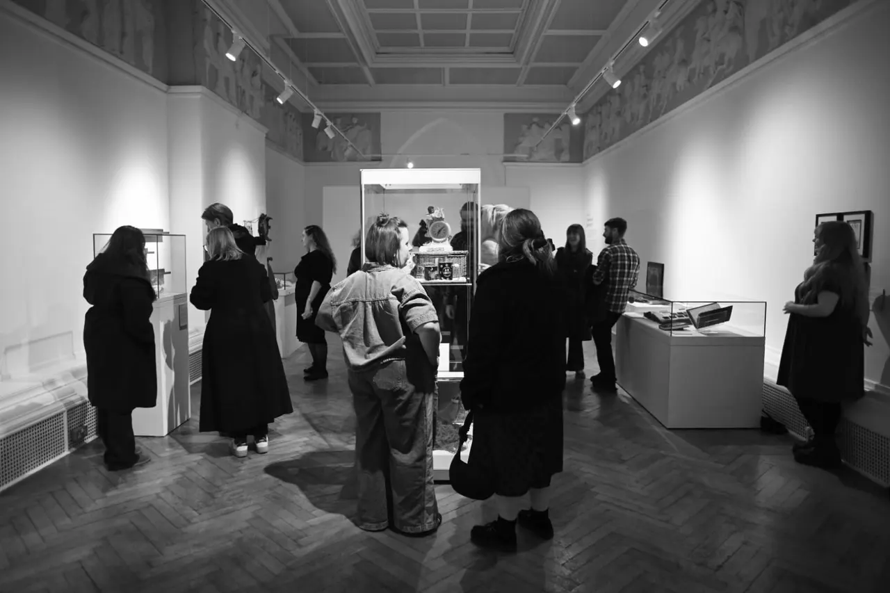 Visitors exploring a modern gallery interior with display cases and illuminated exhibits on white walls.