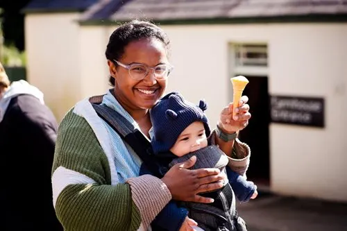 Woman holding a young child, both smiling while holding ice creams outdoors.