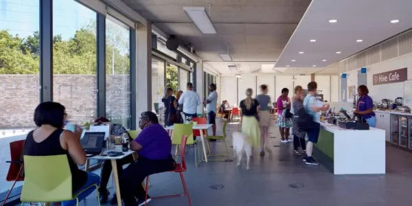 People of various ages socialising and eating in a bright modern café with large windows and colourful seating.