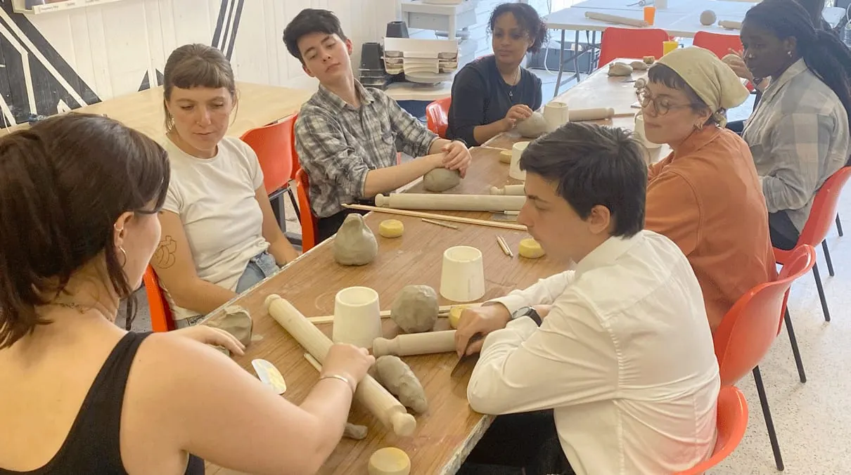 Group of young people working with clay at tables during a pottery workshop indoors.
