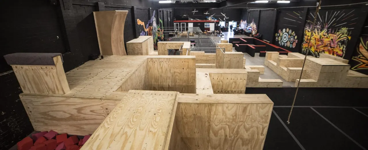 Indoor parkour training facility with wooden obstacles and platforms designed for freerunning practice.