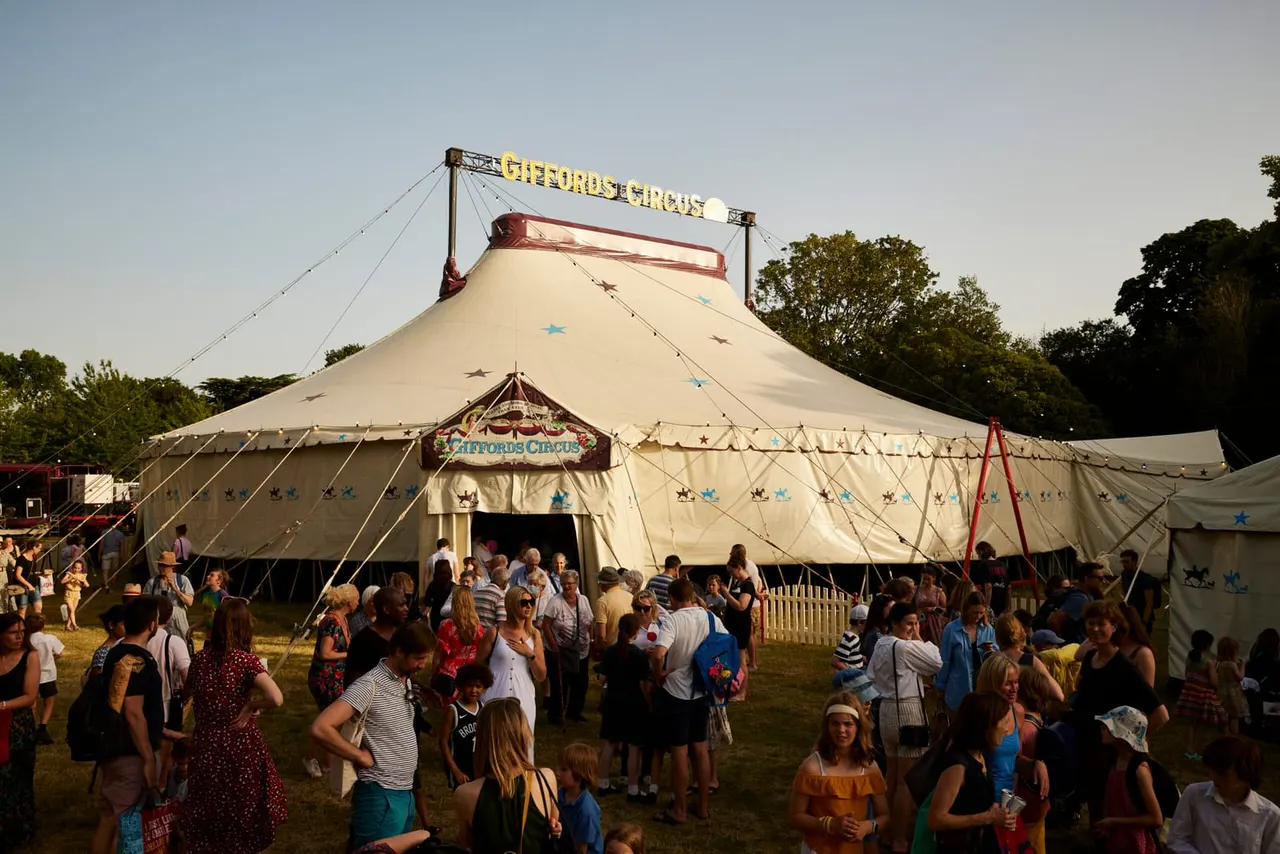 Visitors gather outside a traditional circus big top tent with cream canvas and red trim, decorated with coloured stars.